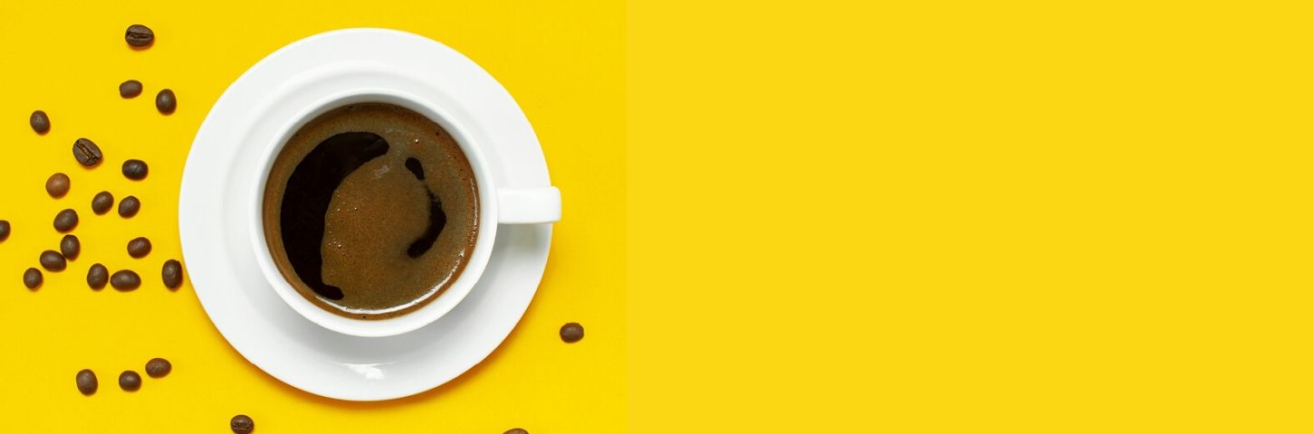 Cup of coffee will spilled beans on bright yellow background