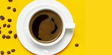 cup of coffee and scattered coffee beans on bright yellow background