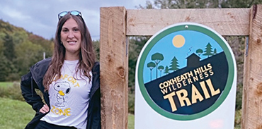 Dr. Saneea Abboud standing next to the Coxheath Hills Wilderness Trail entrance sign
