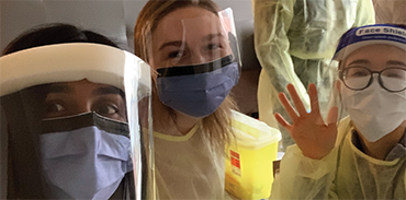 three young female physicians in yellow gowns, masks and face shields