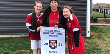 Dr. Everett Fuller with his two daughters on either side holding a championship soccer banner
