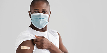 Black man wearing mask and raising his white t-shirt sleeve to show bandage at vaccination site
