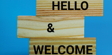 Hello and Welcome written on 3 separate stacked wooden blocks blue background