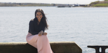 Dr. Priya Koilpillai sitting on a ledge with the ocean behind her