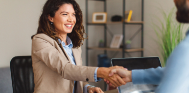female in beige blazer shaking hand of man in blue shirt