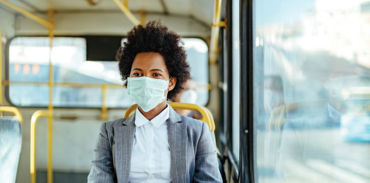 black woman wearing a grey blazer, white blouse and mask while riding a bus