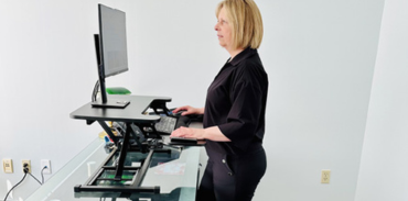 woman with blond hair wearing black pants and blouse while using a walking pad and desk riser