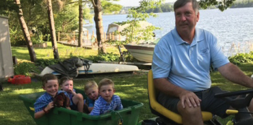 Dr. Robert Oliver towing his four young grandsons in the trailer of a John Deere sit down lawn mower