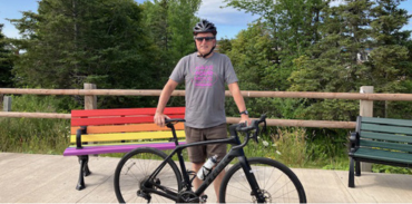 Man standing behind his bicycle with 2 benches and a wooden bench in the backgroun