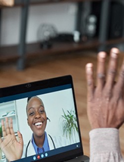 A physican and patient waving to each other during a virtual appointment