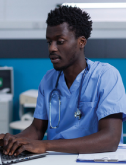 Black male nurse verifying a patient record at a laptop computer