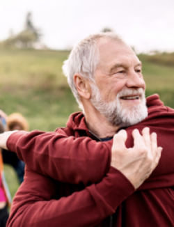 man with grey hair and beard stretching his arms while outdoors