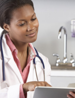 Black female physician wearing a white coat and stethoscope reviewing information on a tablet