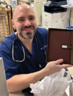 male wearing navy scrubs with a stethoscope around his neck posing with a gift