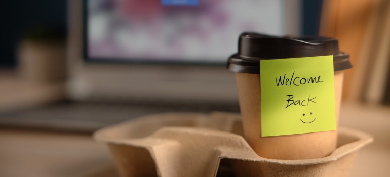 take out coffee cup with yellow note attached with welcome back and a smiley face and laptop computer in the background