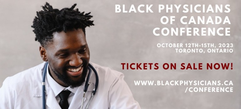 black male physician wearing white lab coat and stethoscope while sitting at a desk and looking at a laptop