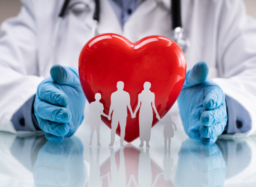 health care worker with blue gloves on holding a paper cut out family with a read heart