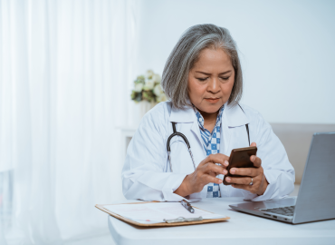 female healthcare worker sits a desk with a cell phone in her hand